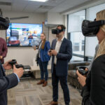 Several professionals stand together in an office wearing VR headsets at a company party